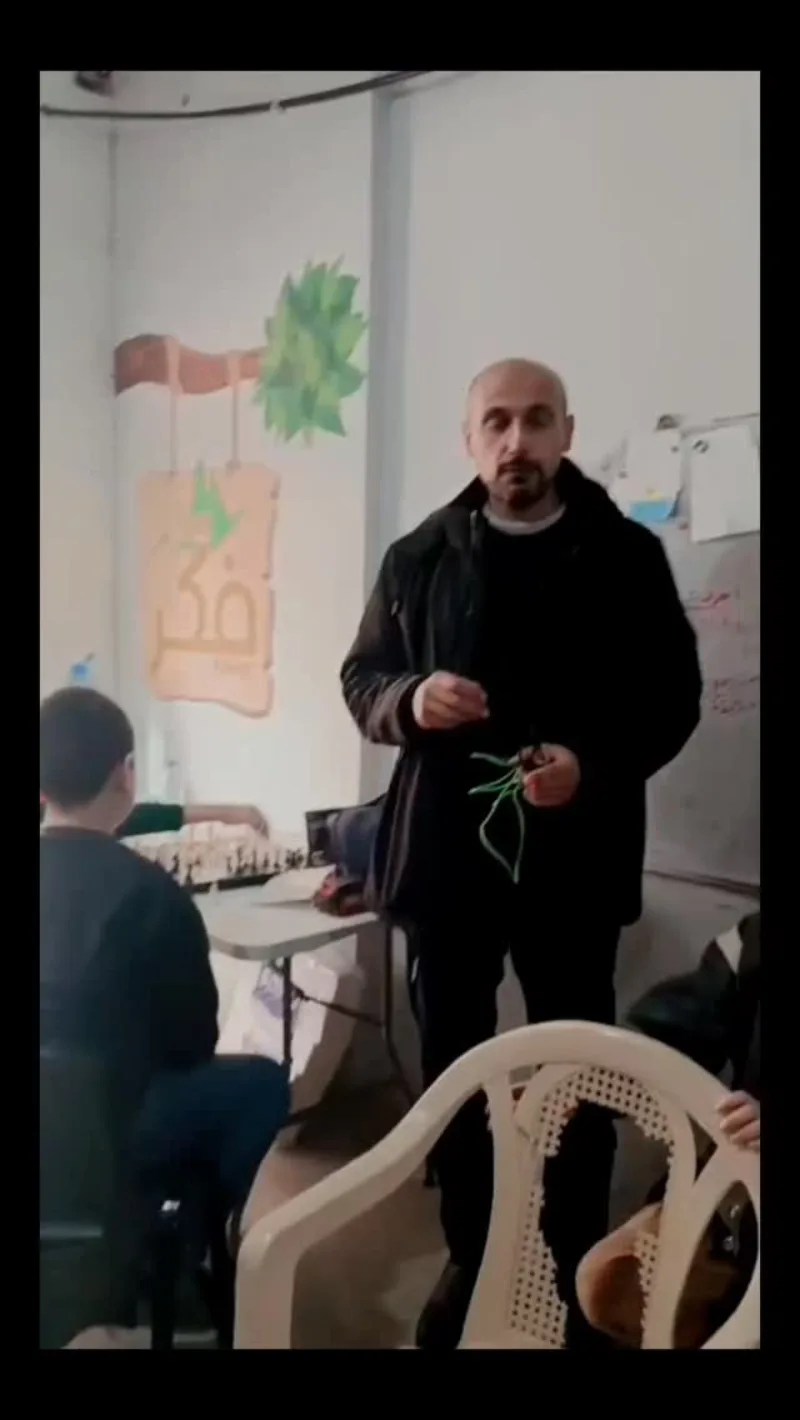 رجل يقف في غرفة صفّ ويتحدث إلى أولاد جالسين حول طاولة.